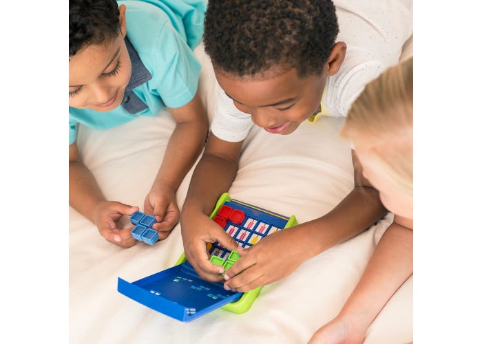 Three children lying on a white bed playing with a colorful toy math game. The toy features blue, green, and red sections with white and blue counters, and the children are actively engaged in solving problems together.